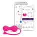 The pink OhMiBod Krush Smart Kegel Fitness Balls with a heart-shaped tail are shown next to two smartphones displaying fitness app interfaces featuring scores, time, and control options. This innovative device uses sensor technology for efficient pelvic floor training.