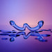 The OhWii Double-Ended Glass Dildo for G-Spot & P-Spot features a curved, abstract design with two upward-facing ends, displayed on a reflective surface with droplets against a gradient purple-orange background.