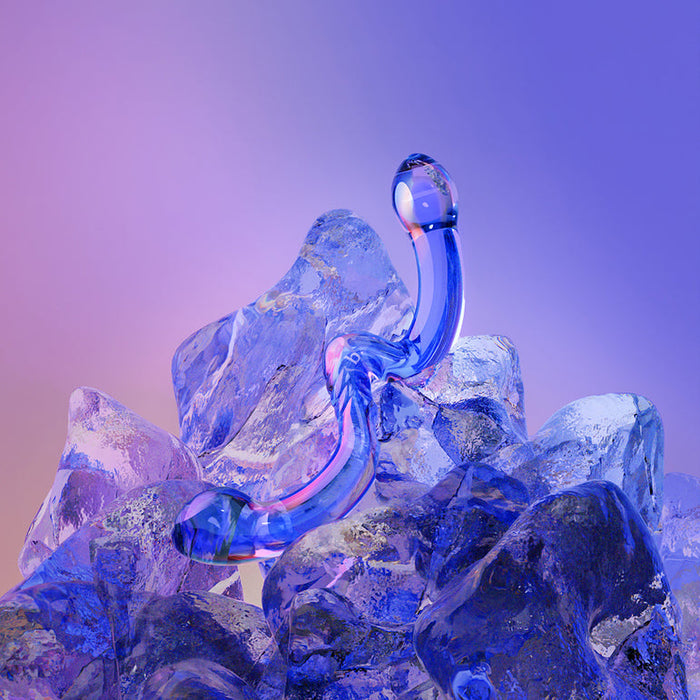 The OhWii Double-Ended Glass Dildo for G-Spot & P-Spot, a translucent blue sculpture with curved ends, rests on large clear ice blocks against a gradient purple and peach background.