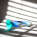 The Opal Dreams Slim 6 Inch Blue Ombre G Spot Dildo, made from silicone with a flared base, rests on a surface with sunlight streaming through window blinds, casting striped shadows. Its shape is perfect for g-spot stimulation.