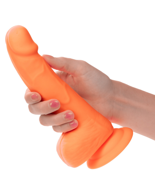 A hand holding a neon-hued delight, an orange, CalExotics Silicone Stud 8 Inch Suction Cup Dildo with a defined head and powerful suction cup base. The object appears to be a sex toy designed to resemble a realistic dildo. The hand is positioned around the middle of the toy.