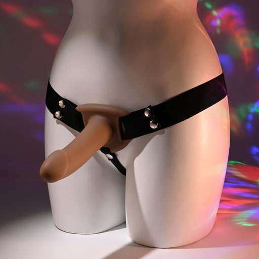 The mannequin's lower half displays the "Our First Hollow Strap-On Dildo + Harness Set - Chocolate," featuring a flexible TPE shaft that mimics real-life texture. Vibrant lighting accentuates its realistic design, ideal for beginners exploring strap-on play.