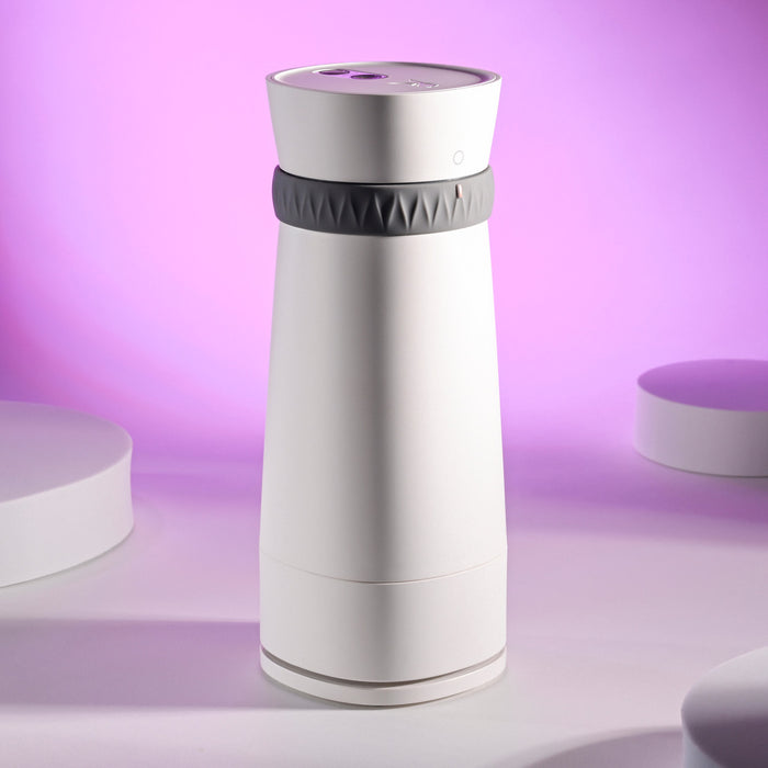 A sleek, modern white Playboy Twist & Stroke Heated Vibrating Stroker with a textured gray band around the top stands on a light surface with a purple-pink gradient background.