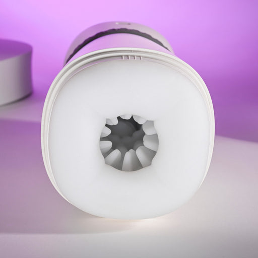A close-up of the white, cylindrical Playboy Twist & Stroke Heated Vibrating Stroker with a soft, textured opening facing the camera, set against a purple background.