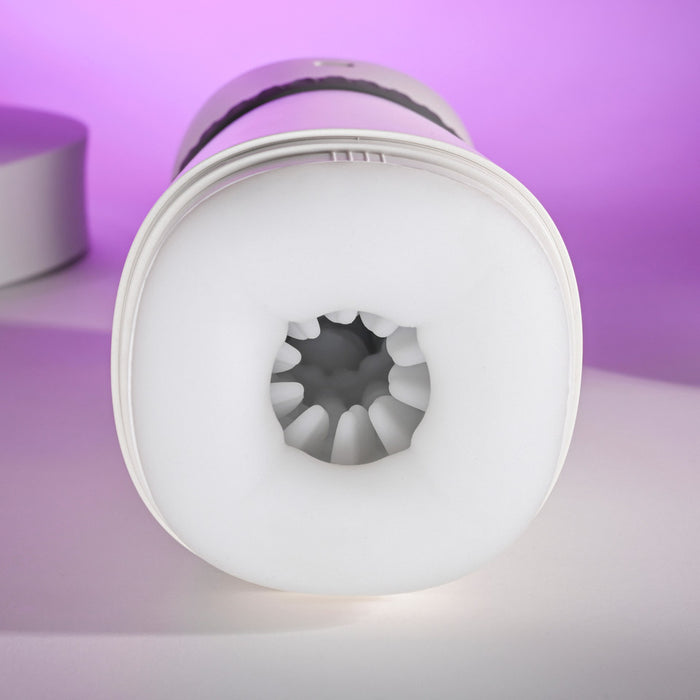A close-up of the white, cylindrical Playboy Twist & Stroke Heated Vibrating Stroker with a soft, textured opening facing the camera, set against a purple background.