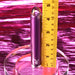 The Amethyst Slim Waterproof Rechargeable Glass Vibrator, featuring a metallic purple finish and the Playboy logo, stands upright on a clear base by a yellow ruler marking its 3.5-inch height, set against a shiny pink background.