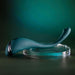 The Pinpoint Perfection Flexible Slim Vibrator, a sleek teal bendable toy with metallic accent, is displayed on a clear circular platform against a green background. Made of body-safe silicone, it offers both style and comfort.