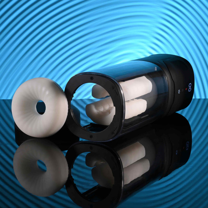 The Playboy Side Piece Heated Sliding Stroker, a black and transparent masturbator with a white donut-shaped sleeve, is shown on a reflective surface against blue ripples, providing realistic heated stroking sensations.