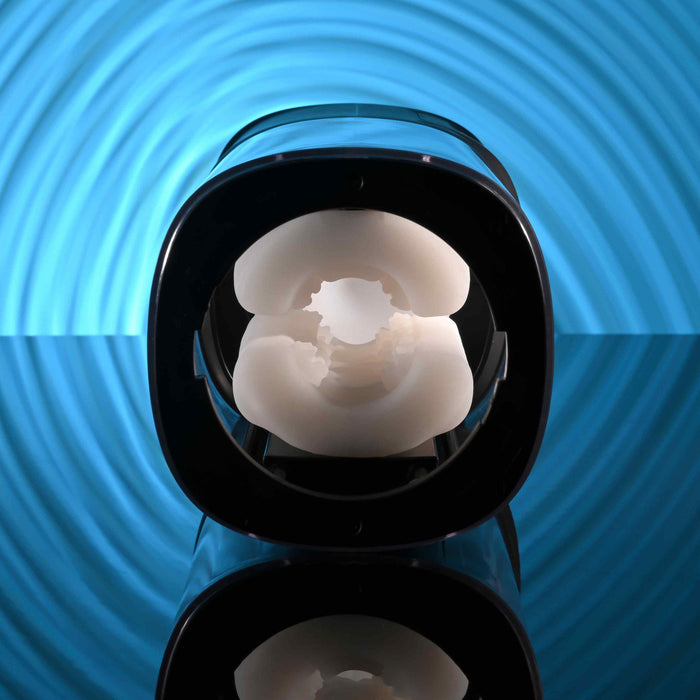 A close-up of the Playboy Side Piece Heated Sliding Stroker, featuring a soft white circular interior and black casing, is set against a blue background with concentric circular patterns.