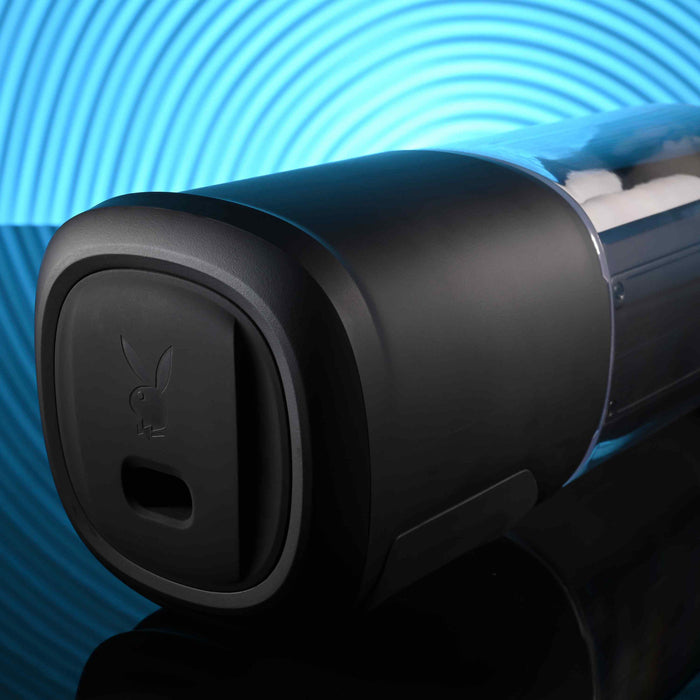 The Playboy Side Piece Heated Sliding Stroker is a sleek black cylindrical toy with a soft, rounded cap featuring the Playboy bunny logo, shown against a vibrant blue circular pattern background.
