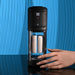 A hand reaches for the Playboy Side Piece Heated Sliding Stroker, a black and transparent vibrating male masturbator with a digital display and two white filters, set on a blue textured background.