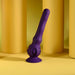 The Wiggle It Silicone Wiggling Vibrator with Suction Cup Base stands upright on a yellow surface, with yellow cylindrical objects in the background.