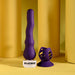 The Wiggle It Silicone Wiggling Vibrator with Suction Cup Base and matching accessory are shown on a yellow surface with cylindrical yellow props. The toy stands upright on its clear base labeled "PLAYBOY" in black letters.