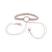 The Peaches 'n Cream Collar and Nipple Clamps by Sportsheets features a beige choker with a central ring that serves as an adjustable collar, linked to two nipple clamps via delicate pearl-embellished chains. The clamps are equipped with white silicone tips, and the design is highlighted by rose gold hardware accents.