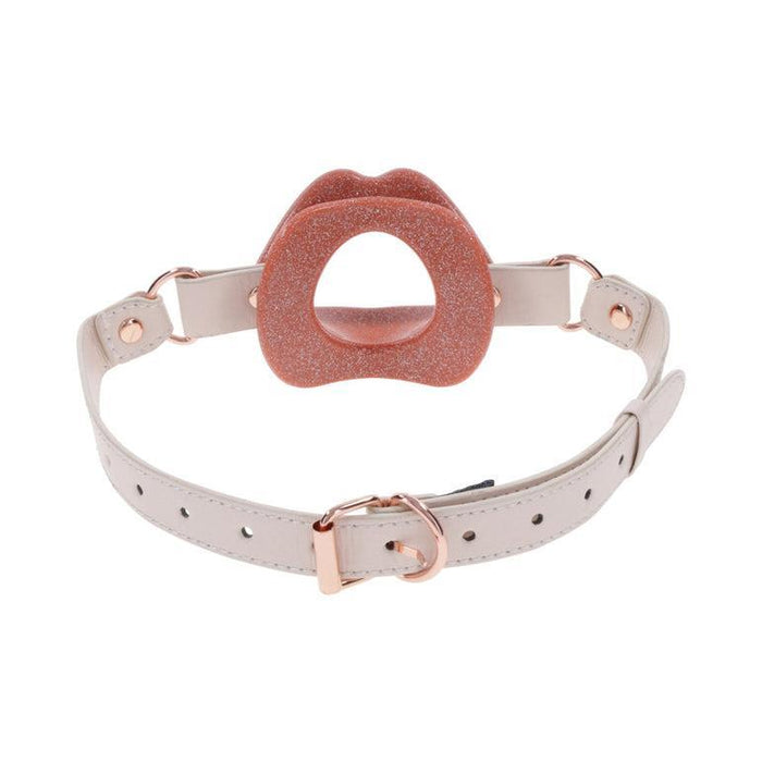 The Peaches 'n Cream Silicone Lips Open Mouth Gag by Sportsheets features a rose gold glittery finish, complemented by a white adjustable strap and rose gold hardware. This silicone piece is crafted in a circular, lip-like shape with a central opening and multiple strap holes for size adjustment, making it ideal for kinky play enthusiasts who appreciate both style and functionality.