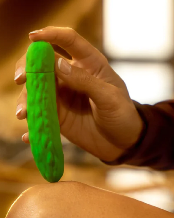 Pickle Emojibator Vibrator held in hand on woman's knee 