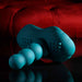 The Playboy Have a Seat Remote Control Grinding Vibrator Pad, a teal silicone personal massager with ribbed texture, rests on a glossy black surface before a red tufted background.