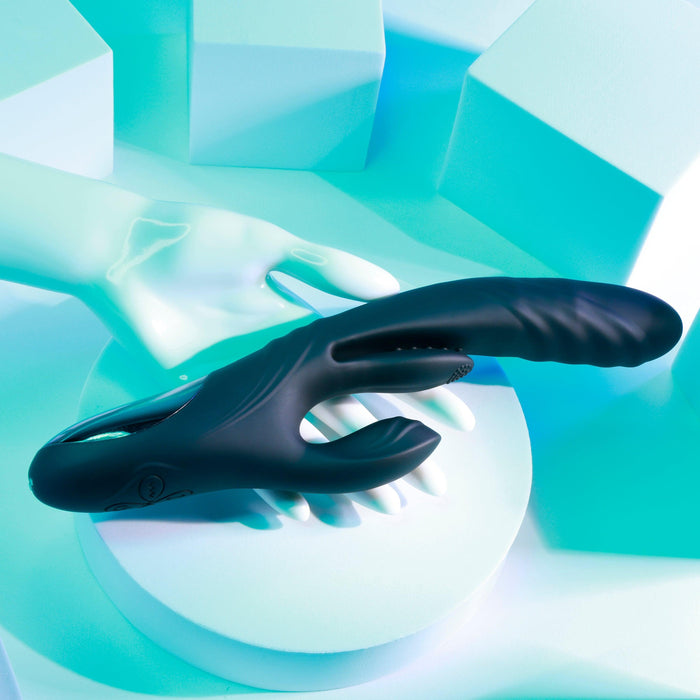 On a pastel blue surface with an abstract background and mannequin hand, the Playboy Rapid Rabbit Thrusting Vibrator with Flapping Shaft is showcased, exuding sleek, modern vibes. This black waterproof vibrator flawlessly merges design and functionality for ultimate satisfaction.
