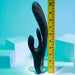 The black Playboy Rapid Rabbit Thrusting Vibrator with Flapping Shaft, a dual-motor adult toy designed for g-spot stimulation, stands upright beside a yellow measuring ruler against light blue geometric shapes. Its flexible and waterproof design enhances pleasure.