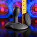 The Playboy Sittin' & Spinnin' Hands Free G-Spot Vibrating Grinder Pad, in black silicone with a remote control, stands upright beside a yellow ruler against an abstract background with red and blue patterns.