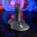 The Playboy Sittin' & Spinnin' Hands Free G-Spot Vibrating Grinder Pad, a sleek gray silicone toy with buttons and a curved, ribbed design, stands upright on a reflective surface amid swirling colorful lights and an abstract background.