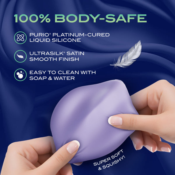 Hands squeeze the Pulse Pad Squishy Silicone External Vibrator with Remote, violet-hued on a silky blue background. Features: 100% body-safe platinum-cured liquid silicone, satin smooth finish, easy to clean with soap & water.