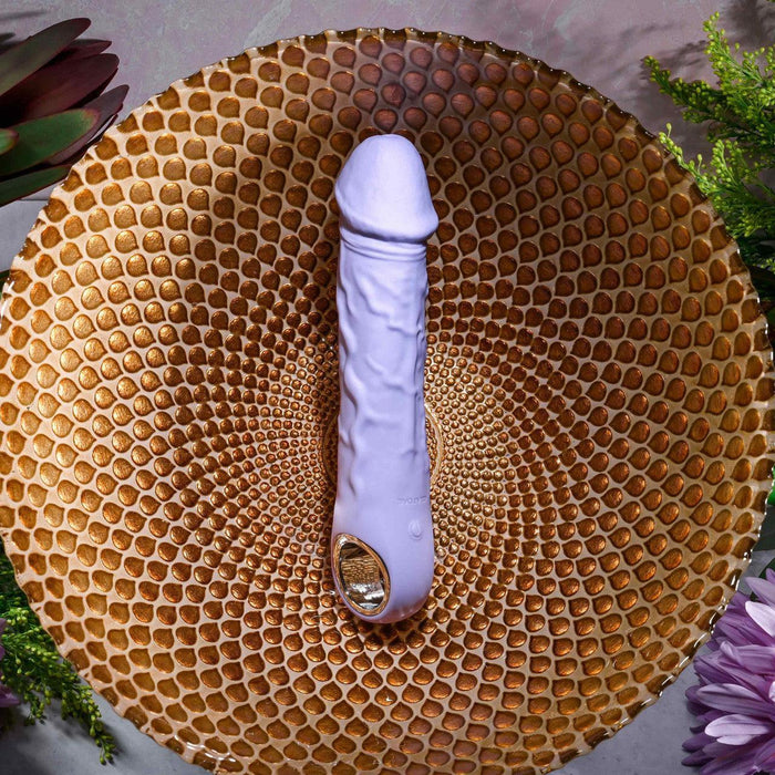 Lavender silicone vibrating dildo with realistic veins and a metallic finger loop base on a gold decorative plate.