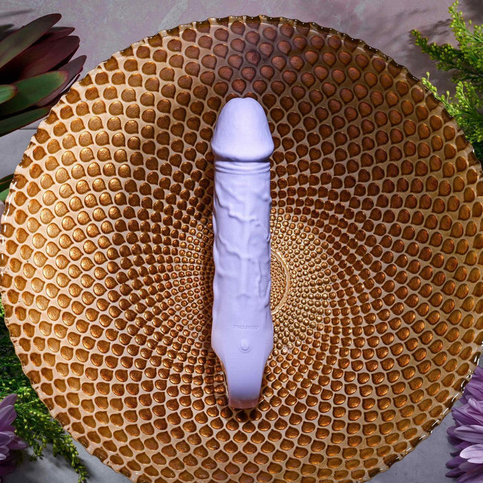 Lavender silicone vibrating dildo with realistic veins and a base finger loop, displayed on a gold textured bowl.