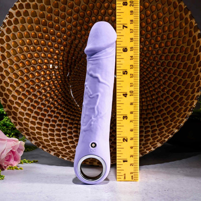 Lavender silicone vibrating dildo with veiny texture, finger loop, and magnetic charging port next to a ruler.