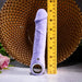 Lavender silicone vibrating dildo with veiny texture, finger loop, and magnetic charging port next to a ruler.