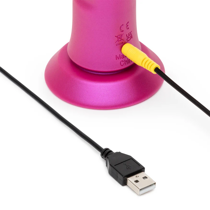 Close-up of the ROMP Jiggle Thrusting Vibrator with Suction Base in pink, showing the device's base with a yellow audio jack plugged in and a black USB cable nearby on a white background.