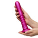 Two hands hold the ROMP Jiggle Thrusting Vibrator with Suction Base, a large metallic pink ribbed silicone toy, vertically positioned against a plain white background.