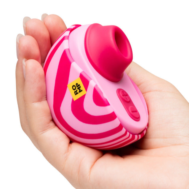 A hand holds the Romp Spin Small Discreet Pleasure Air Clitoral Stimulator—a pink and white striped, travel-size device with a round opening, two buttons, and a yellow "RIP" sticker.