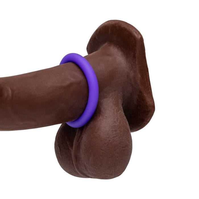 The Romp Remix Cock Ring Trio features a brown, body-safe silicone dildo with a purple cock ring at its base above two testicle shapes, all shown isolated on a white background.