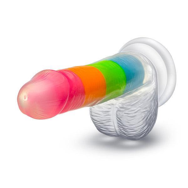 The Rainbow Rave Slim Glow in the Dark 6.5 Inch Silicone Dildo features a realistic, rainbow-striped design, textured detail, a translucent white suction base, and is strap-on harness compatible for versatile play.