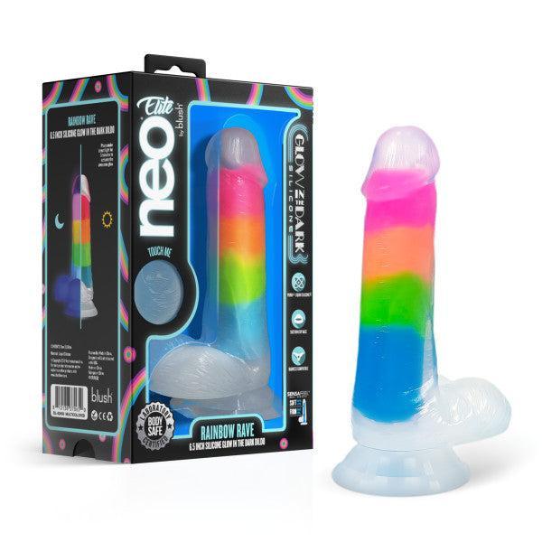 The Rainbow Rave Slim Glow in the Dark 6.5 Inch Silicone Dildo, featuring rainbow stripes, a suction base, and body-safe silicone that is strap-on harness compatible, is displayed beside its detail-rich packaging.
