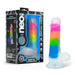 The Rainbow Rave Slim Glow in the Dark 6.5 Inch Silicone Dildo, featuring rainbow stripes, a suction base, and body-safe silicone that is strap-on harness compatible, is displayed beside its detail-rich packaging.