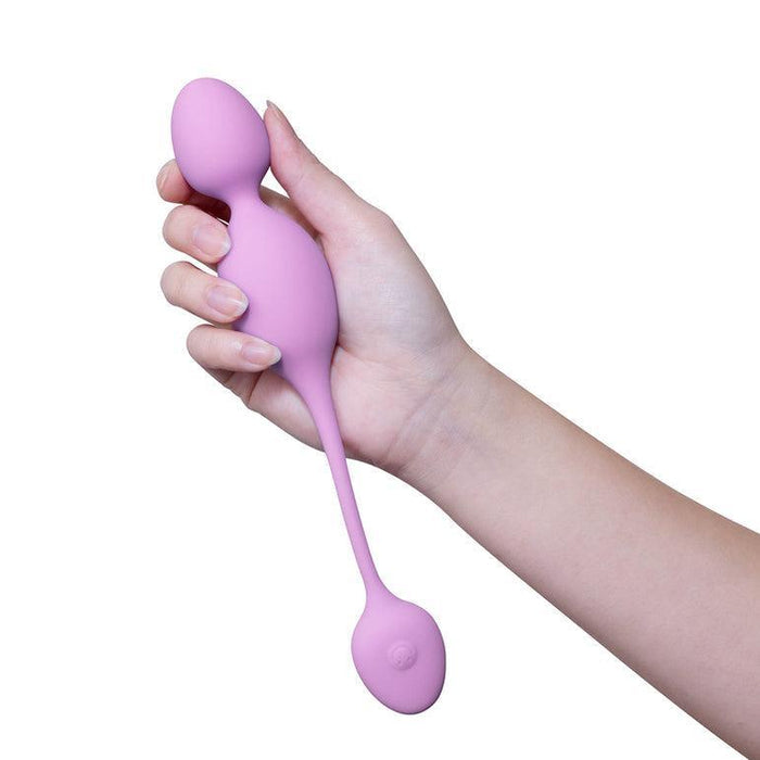 A person holds the pink Raine Vibrating Kegel Ball with Remote Control, featuring two bulbous ends and a long connector. Designed for pelvic floor strengthening, it rests in a hand against a neutral background.