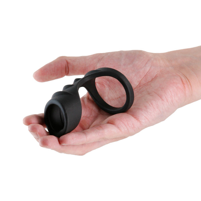 A hand holds the Renegade Bolster Silicone Penis Support Harness—black, with two loops—designed for erection support, photographed against a plain white background.