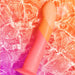The Romp Dizi Ultra Smooth 7 Inch G-Spot Dildo with suction cup, in pink and orange, is harness compatible and lies in shallow water with ripples and reflections on a vibrant pink and orange background.
