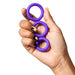 A hand with black and yellow painted nails holds the Romp Remix Easy to Use Cock Ring Trio—three stretchy silicone rings of different sizes—against a white background.