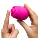 A person holds the Romp Rose 2 Pleasure Air Clitoris Stimulator—a pink, rose-shaped silicone toy—between their hands, pointing toward its opening. The white background highlights its design for clitoral stimulation.
