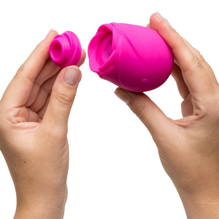 Two hands hold the Romp Rose 2 Pleasure Air Clitoris Stimulator, a pink silicone rose-shaped device with one hand on the main unit and the other showing its detachable silicone attachment, set against a white background.
