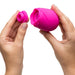 Two hands hold the Romp Rose 2 Pleasure Air Clitoris Stimulator, a pink silicone rose-shaped device with one hand on the main unit and the other showing its detachable silicone attachment, set against a white background.