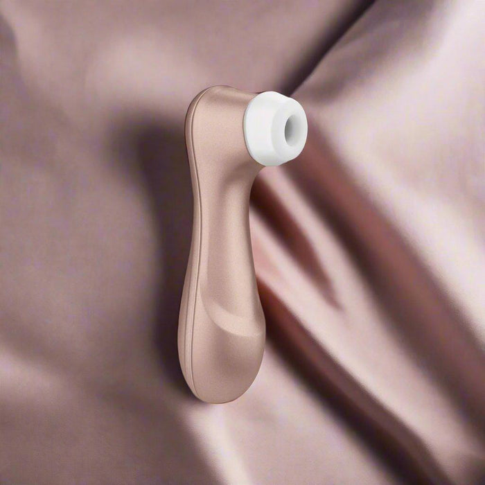 The rose gold Satisfyer Pro 2 Waterproof Pressure Wave Clitoral Stimulator with a white tip rests on shimmering mauve fabric, featuring advanced pressure wave technology for enhanced pleasure.