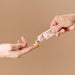 Two hands are shown; one squeezes a pink tube labeled "SEX" to dispense yellowish Sex au Naturel Vulva Balm Soothing Moisturizer onto the other’s fingers, with a plain beige background.