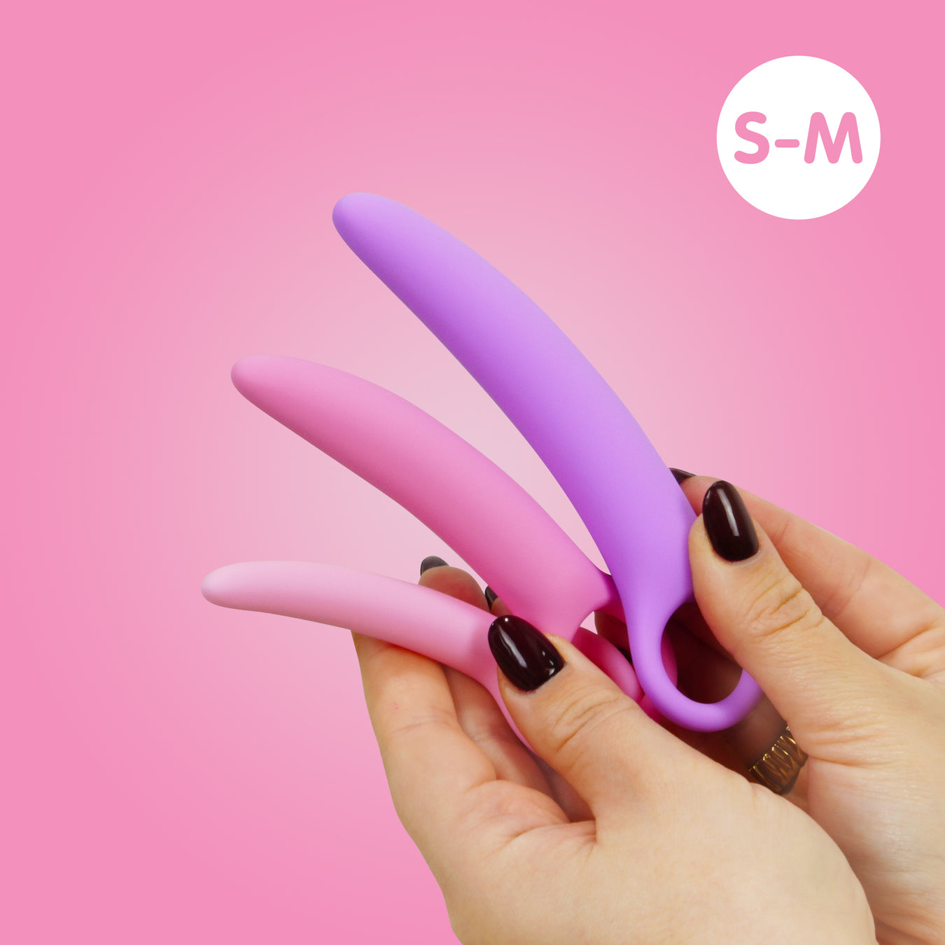 A hand with dark nail polish holds three pastel-colored silicone dilators in increasing sizes against a pink background, with a white circle labeled “S-M” in the corner.