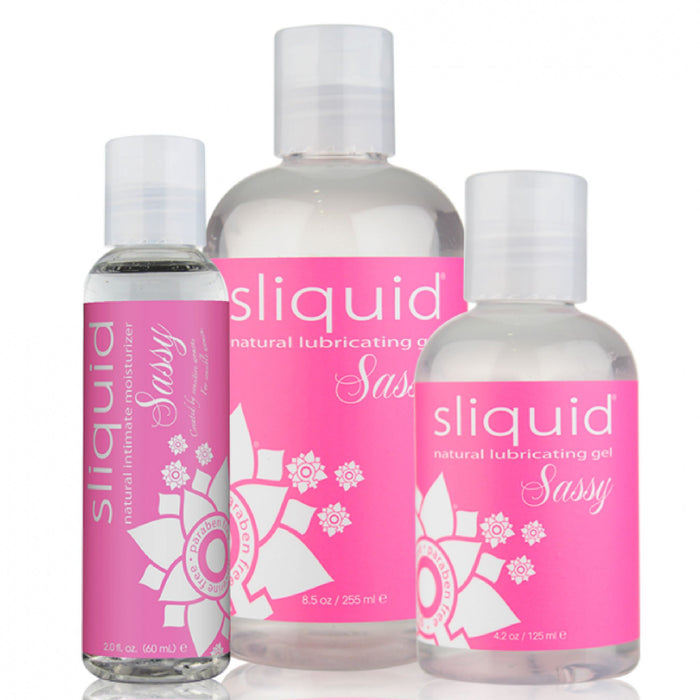 Displayed are three bottles of Sliquid Naturals Sassy Water Based Anal Lube in sizes 8.5 oz, 4.2 oz, and 2 oz, each with a pink label featuring a white floral design and text emphasizing the vegan-friendly and glycerin-free formula.