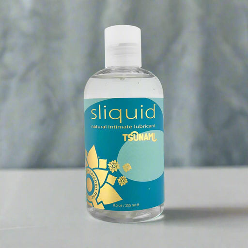 An 8.5 oz (255 ml) bottle of Sliquid Tsunami Ultra Thick Water Based Lubricant features water-based carrageenan, a teal label with abstract sun and waves, a white flip-top cap, and is set against a blurred background for added mystery.