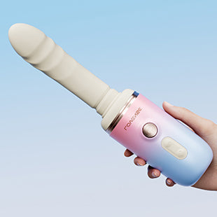 A hand holds the Spinel App-Controlled, Multi-Attachment Thrusting, Vibrating & Heating Dildo Machine, shown in pastel pink and blue with a textured beige cylindrical attachment, set against a light blue background.